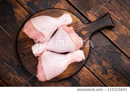 Uncooked poultry drumsticks, raw chicken legs ideal for your favorite recipes, waiting to be seasoned and cooked to perfection. wooden background. top view Uncooked poultry drumsticks, raw chicken legs ideal for your favorite recipes, waiting to be seasoned and cooked to perfection. wooden background. top view 133325643