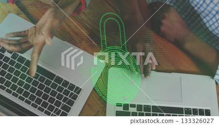 Discussing risks, two IT colleagues gesturing over laptops on wood desk, with green padlock overlay Discussing risks, two IT colleagues gesturing over laptops on wood desk, with green padlock overlay 133326027