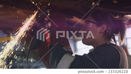 Mechanic grinding chassis with angle grinder in workshop, sparks flying, wearing gloves, copy space 133326228