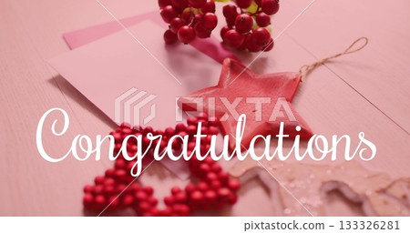 Arranging red wooden star ornament with twine loop, beaded star, berry sprigs, pink card on desk 133326281