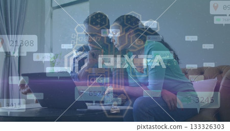 Analyzing couple exploring floating data overlays on laptop in living room, with sofa and plant 133326303