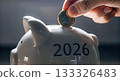 Hand putting gold coin into white piggy bank with number 2026 text close up saving money future financial plan investment budget 133326483