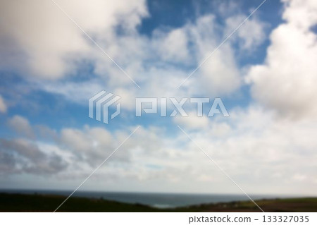Blurred coastline featuring gray clouds filling sky, ocean horizon meeting green and brown farmland 133327035