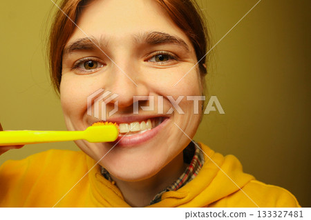 A bright close up of a woman with a radiant smile demonstrating good oral health. She is actively brushing her teeth with a toothbrush, with vibrant yellow accents A bright close up of a woman with a radiant smile demonstrating good oral health. She is actively brushing her teeth with a toothbrush, with vibrant yellow accents 133327481