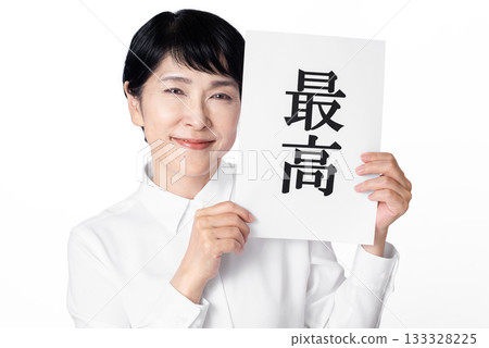 A senior woman wearing a white shirt smiling and holding a piece of paper with the word "best" written on it in both hands A senior woman wearing a white shirt smiling and holding a piece of paper with the word "best" written on it in both hands 133328225