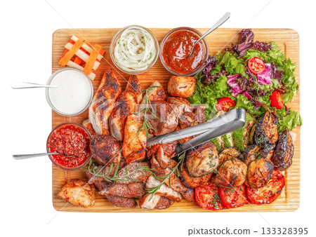 Mixed grilled meat with vegetables, fresh salad and assorted sauces served on wooden board, top view food composition for advertising or restaurant menu design 133328395