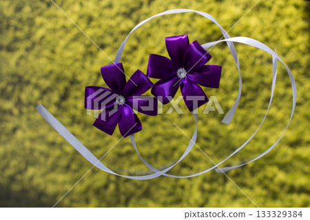 Two purple corsages with rhinestones resting on white ribbons for wedding ceremony Two purple corsages with rhinestones resting on white ribbons for wedding ceremony 133329384