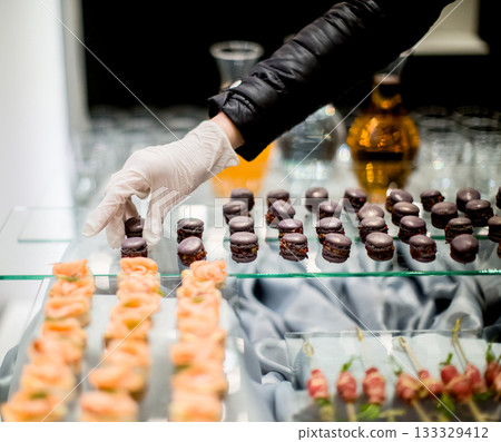 Caterer arranging delicious macarons on glass tray for wedding reception Caterer arranging delicious macarons on glass tray for wedding reception 133329412