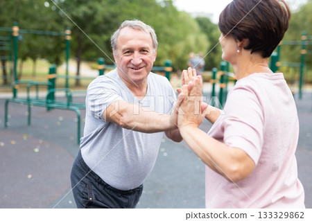 Friendly family couple doing gymnastic exercises together in summer city park Friendly family couple doing gymnastic exercises together in summer city park 133329862