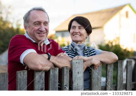 Positive mature man and woman standing near fence in garden Positive mature man and woman standing near fence in garden 133329871