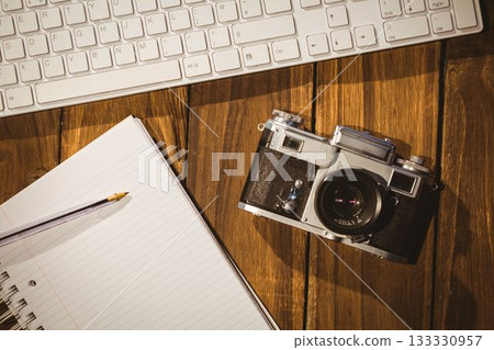 Vintage film camera is resting beside keyboard and notebook with pencil in flat design workspace 133330957