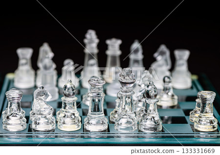 glass, transparent chess pieces on a checkerboard, selective focus, close-up, isolated on black 133331669