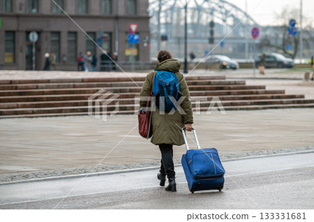 A tourist with a backpack pulls a suitcase on wheels down the street, rear view A tourist with a backpack pulls a suitcase on wheels down the street, rear view 133331681