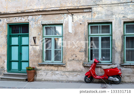Red vintage scooter on the sidewalk in front of an old brick house 133331718