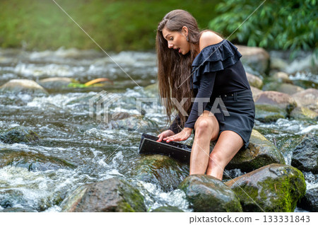 female freelancer sitting on a rock in the river and dropping her laptop into the water female freelancer sitting on a rock in the river and dropping her laptop into the water 133331843