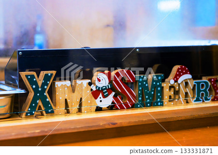Closeup of colorful Xmas merry decorative letters placed on a wooden counter at a christmas market food stall, with warm steam rising in the background. Closeup of colorful Xmas merry decorative letters placed on a wooden counter at a christmas market food stall, with warm steam rising in the background. 133331871