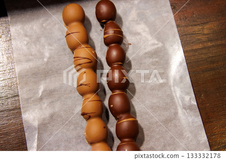 Closeup of two milk and dark chocolate coated grape dessert skewers at a festive christmas or advent market. Closeup of two milk and dark chocolate coated grape dessert skewers at a festive christmas or advent market. 133332178