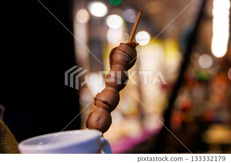 Chocolate dessert at a night Christmas market. Choco covered grape skewer with soft bokeh lights in the background, creating a warm, festive atmosphere, Chocolate dessert at a night Christmas market. Choco covered grape skewer with soft bokeh lights in the background, creating a warm, festive atmosphere, 133332179