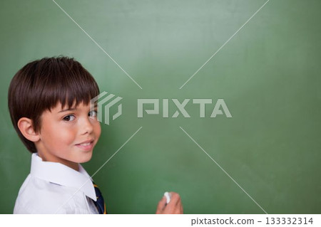 schoolboy is standing in flat design classroom holding white chalk against blank green chalkboard 133332314