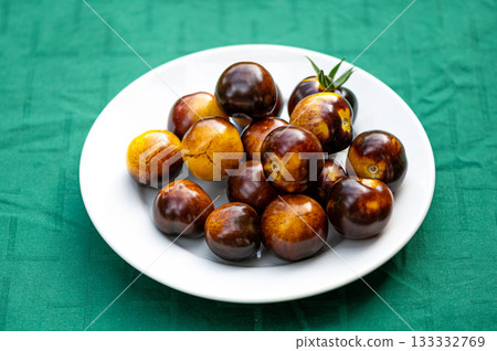 fresh cherry tomatoes of different varieties on a plate on the blurred background, closeup 133332769