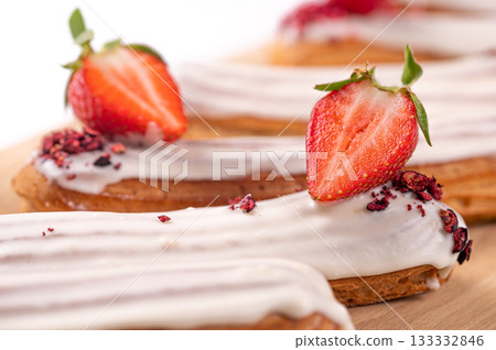 delicious eclair with icing and whipped cream filling, French dessert with strawberries, closeup 133332846
