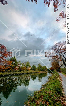 Tranquil waterway bordered by bright trees and drifting leaves Tranquil waterway bordered by bright trees and drifting leaves 133332877