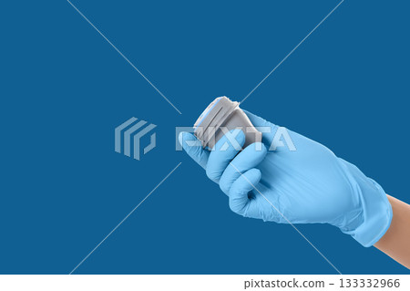 Gloved hand holding a small container for medical use 133332966