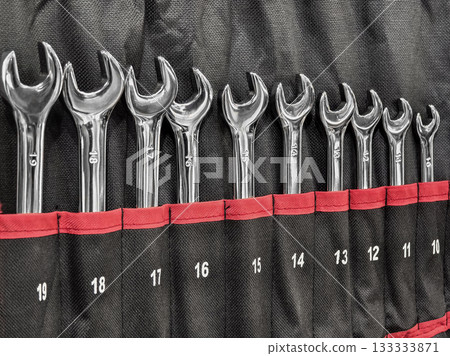 Array of shiny wrenches neatly organized in a black and red tool pouch at a workshop 133333871