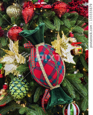 Colorful decorative ornament resembling candy on a Christmas tree filled with festive decorations and lights 133333879