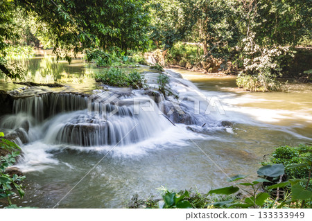 A small waterfall cascades over layered rocks surrounded by trees, with the water flowing in shallow steps into a wider pool. A small waterfall cascades over layered rocks surrounded by trees, with the water flowing in shallow steps into a wider pool. 133333949