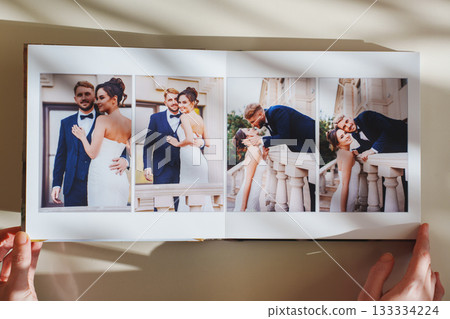 Female hands flipping through a photo book with wedding photos on a white table 133334224