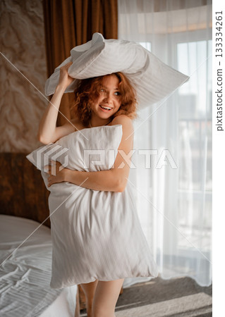Cheerful girl enjoys morning in bedroom with white soft pillows 133334261