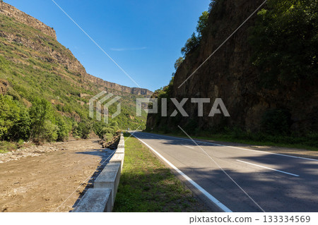 A winding road cuts through a canyon, flanked by tall rock walls and lush greenery A winding road cuts through a canyon, flanked by tall rock walls and lush greenery 133334569