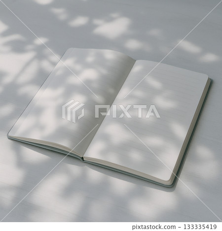 Still life of a notebook and pen cast by the shadow of sunlight filtering through the trees 133335419
