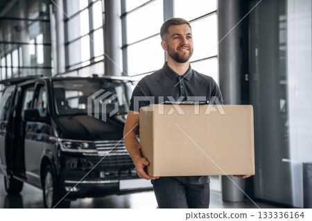 With a box, smiling. Delivery man or loader is near the car 133336164