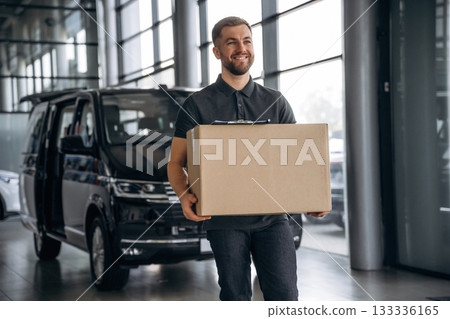 With a box, smiling. Delivery man or loader is near the car 133336165