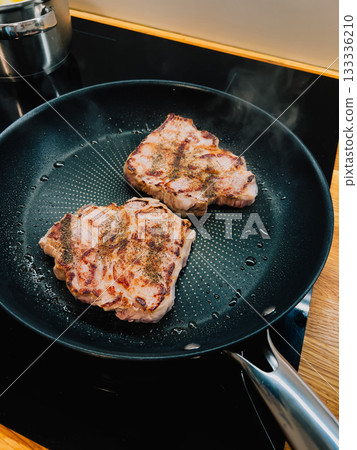 Two seasoned pork neck steaks are frying in hot pan on modern induction stove, creating delicious aroma and steam, classic culinary scene. Sizzling pork neck steaks browning in cast iron skillet Two seasoned pork neck steaks are frying in hot pan on modern induction stove, creating delicious aroma and steam, classic culinary scene. Sizzling pork neck steaks browning in cast iron skillet 133336210