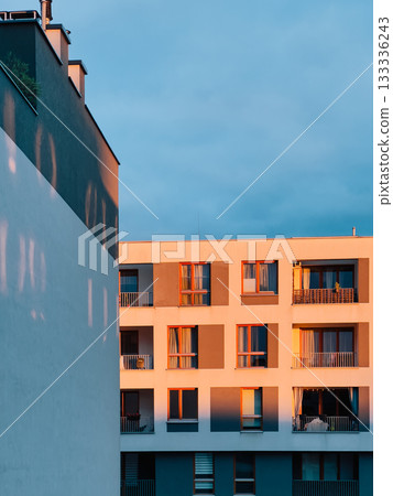 Warm sunset light illuminating modern residential building facade, casting long shadows on adjacent wall, creating vibrant urban cityscape at dusk. Residential architecture, urban facade, golden hour 133336243