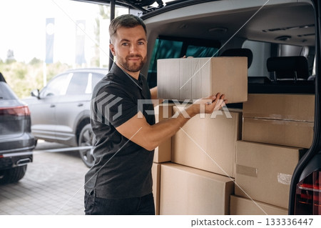 Holding the packed product in hands. Delivery man or loader is near the car with a box Holding the packed product in hands. Delivery man or loader is near the car with a box 133336447
