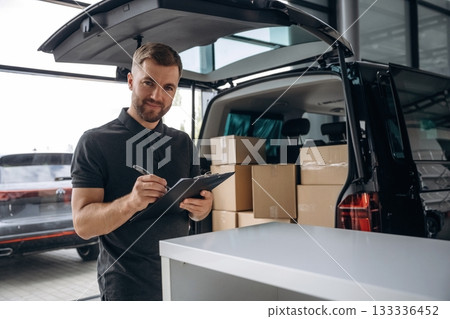 Data in the notepad. Delivery man or loader is near the car with a box 133336452
