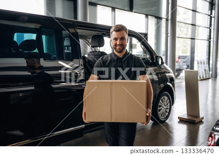 Big order, holding the box. Delivery man or loader is near the car with 133336470