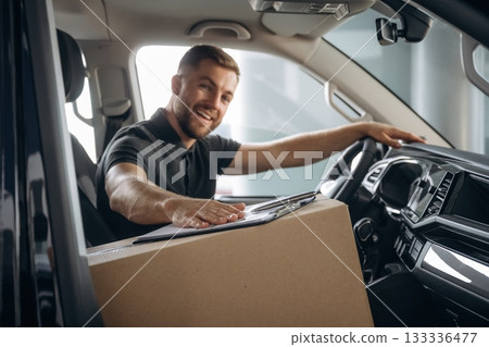 Looking at the camera, smiling. The delivery man or a loader is in the car with box Looking at the camera, smiling. The delivery man or a loader is in the car with box 133336477