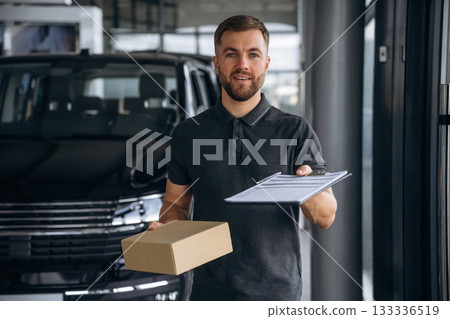 Front view, standing. Delivery man or loader is near the car with a box Front view, standing. Delivery man or loader is near the car with a box 133336519