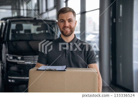Smiling, positive facial expression. Delivery man or loader is near the car with a box Smiling, positive facial expression. Delivery man or loader is near the car with a box 133336524