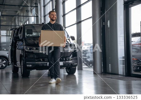 Smiling, positive facial expression. Delivery man or loader is near the car with a box Smiling, positive facial expression. Delivery man or loader is near the car with a box 133336525