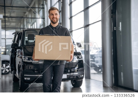 Smiling, positive facial expression. Delivery man or loader is near the car with a box Smiling, positive facial expression. Delivery man or loader is near the car with a box 133336526