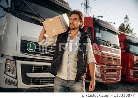 Delivery is on the way, with box. Truck driver is near the transport outdoors Delivery is on the way, with box. Truck driver is near the transport outdoors 133336877