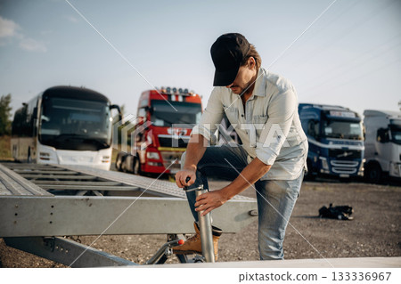 In the casual clothes and in black cap. Truck driver is near the transport outdoors In the casual clothes and in black cap. Truck driver is near the transport outdoors 133336967