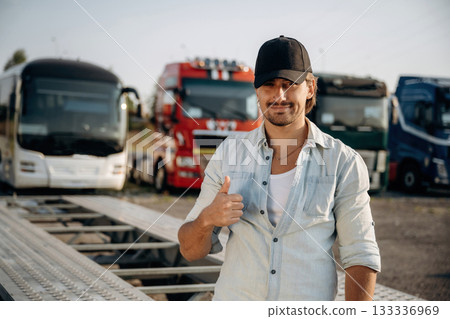 Thumb up, standing. Truck driver is near the transport outdoors Thumb up, standing. Truck driver is near the transport outdoors 133336969