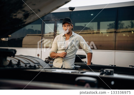 Looking at the truck, smoking. Driver is near the transport outdoors 133336975